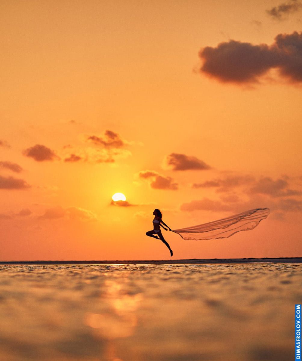 Foto criativa de praia ao pôr do sol com uma mulher pulando com um longo véu