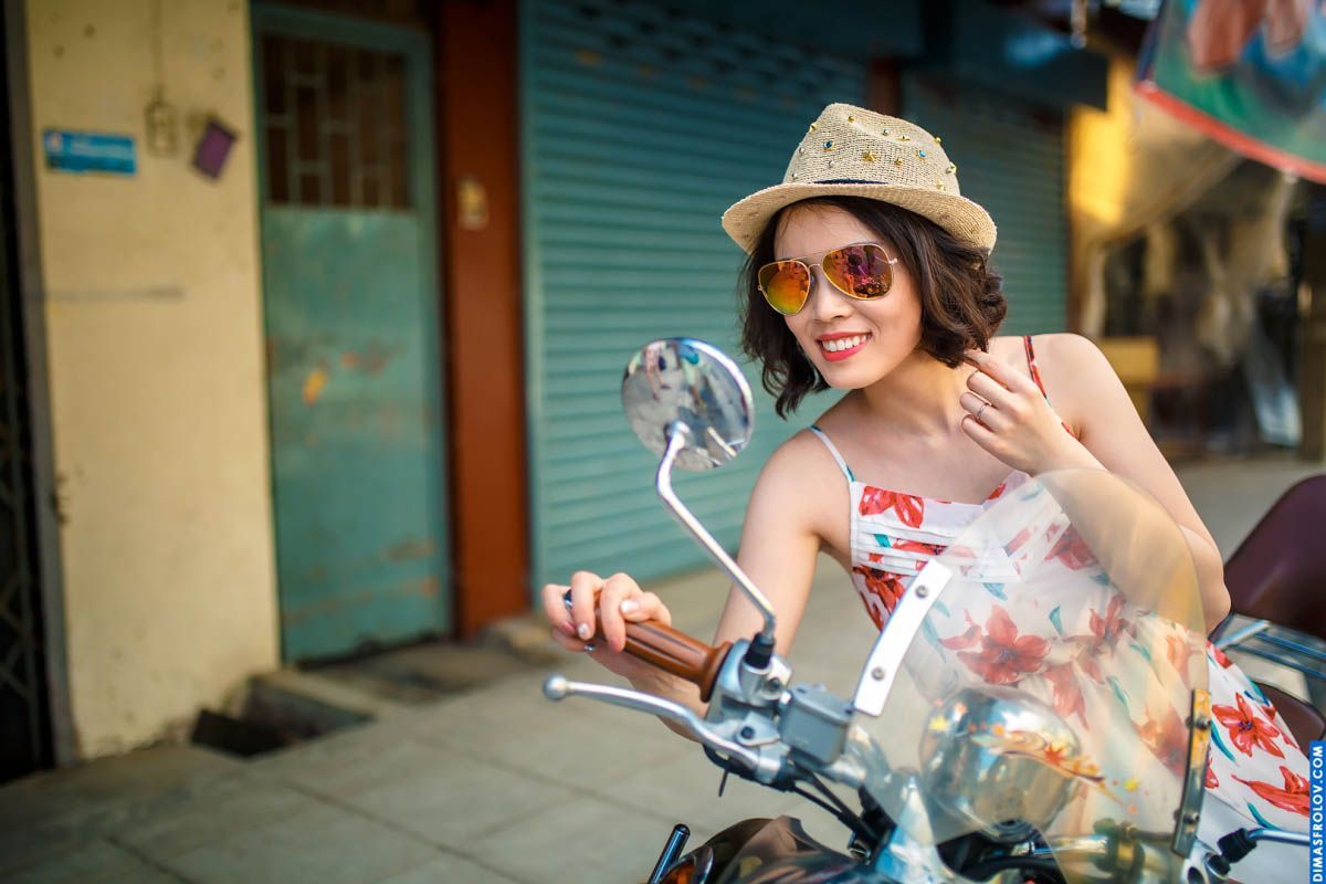 Retrato de viagem de uma mulher estilosa em um vestido floral, com chapéu e óculos de sol, em uma scooter