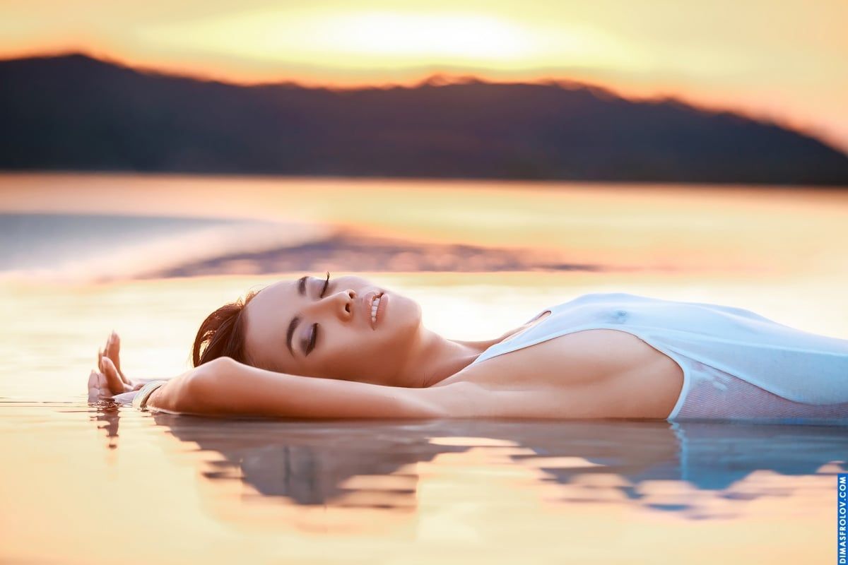 Foto minimalista de uma mulher relaxando em uma piscina infinita ao pôr do sol