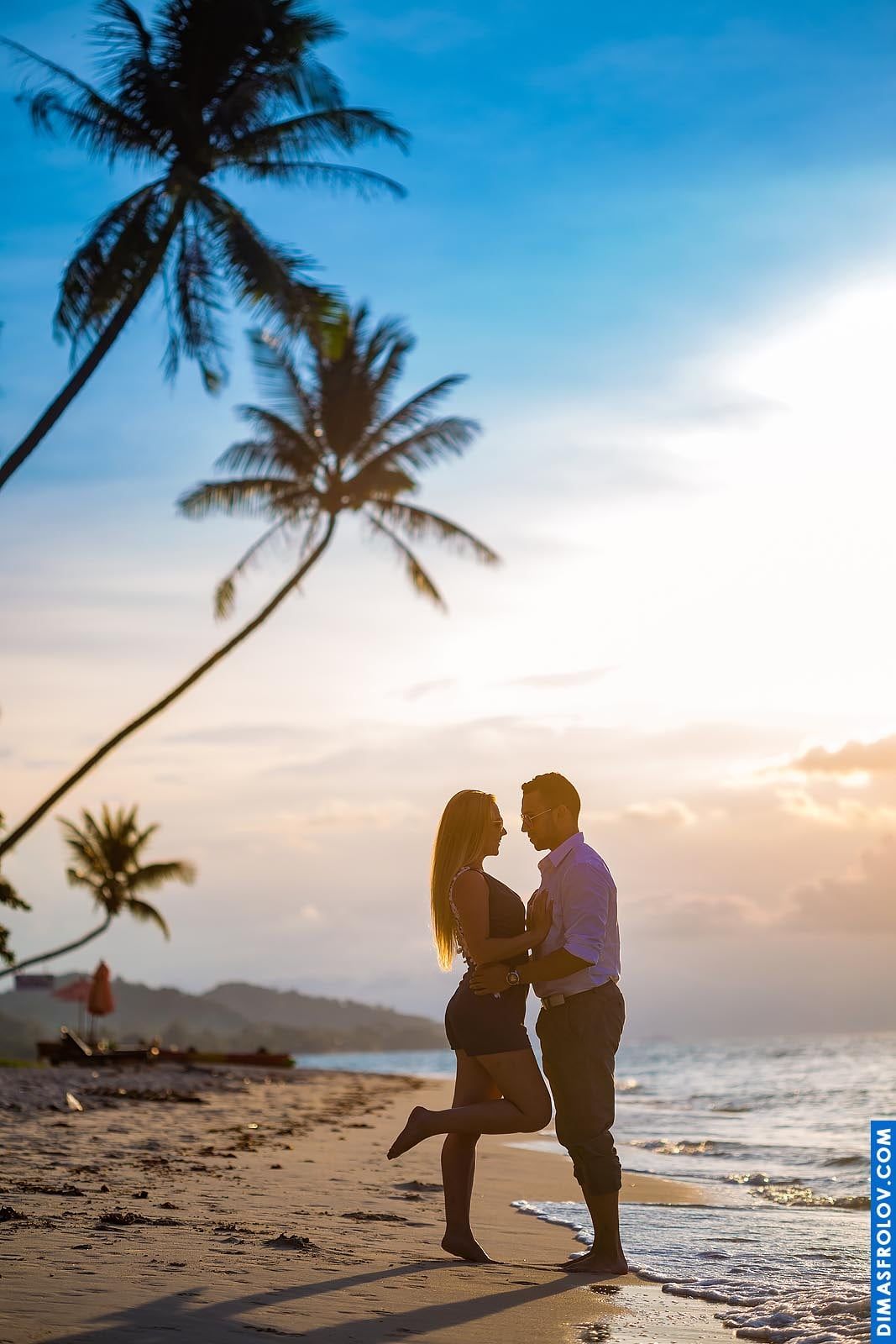 Passionate couple kiss by the sea at sunset with tall palm trees around