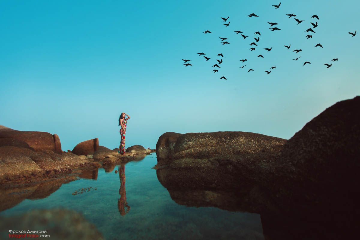Conceptual photo shoot of a girl standing on rocks with flying birds in the sky