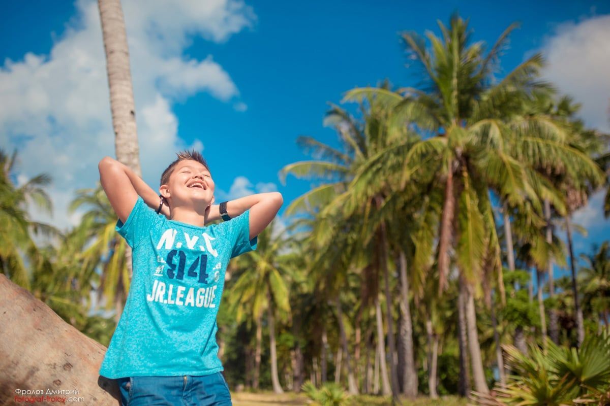 Happy boy photo — arms wide open, enjoying the palm-lined view