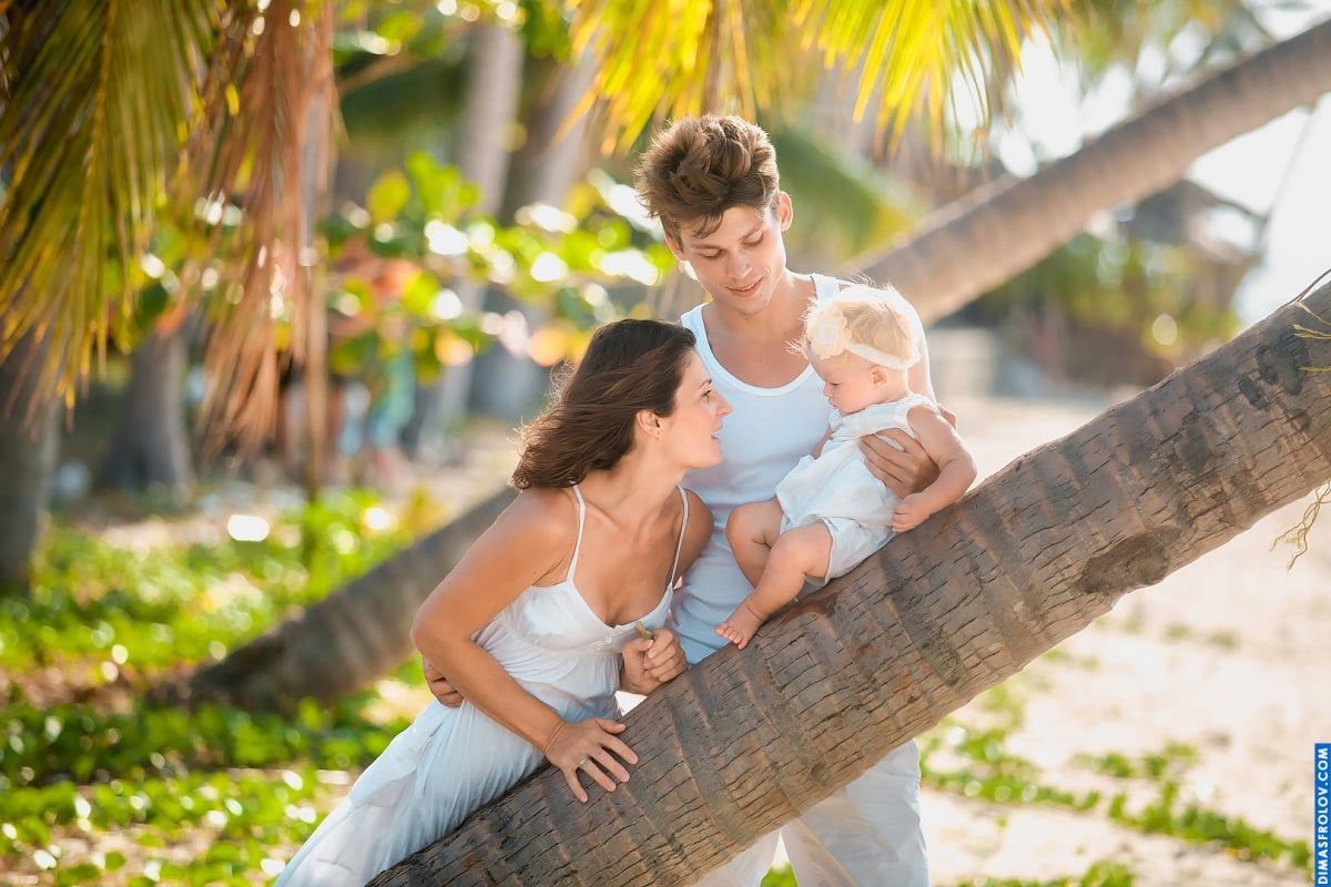 Lifestyle family photo with baby under a palm — natural beach moment