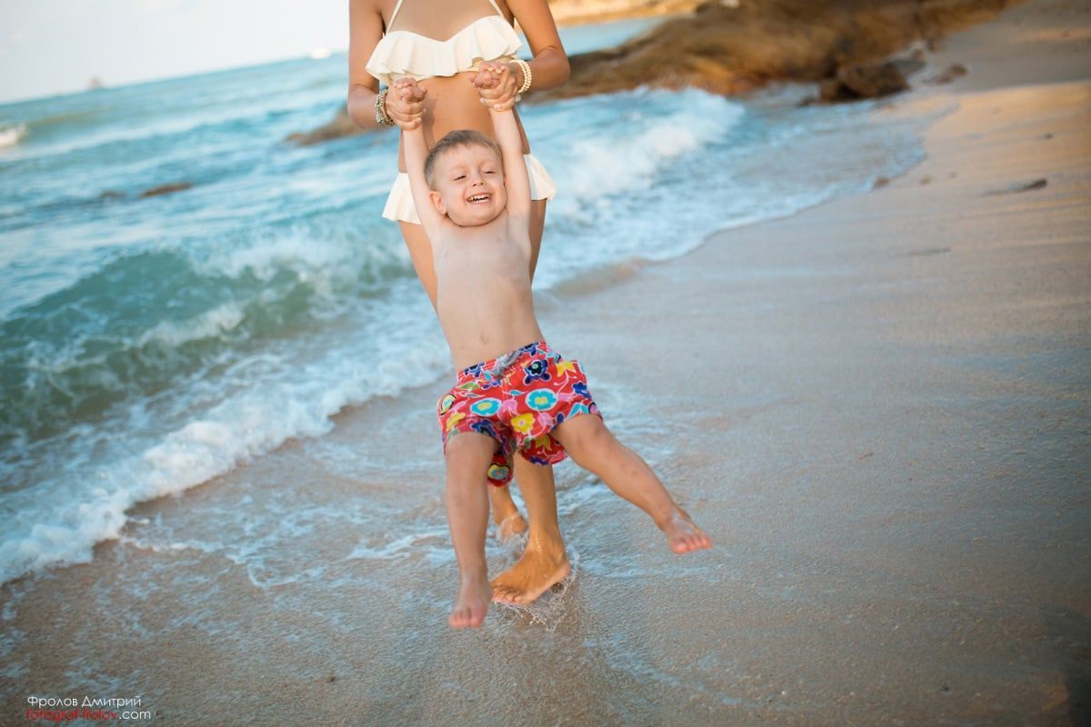 Laughing boy swinging by the sea during a joyful photo shoot