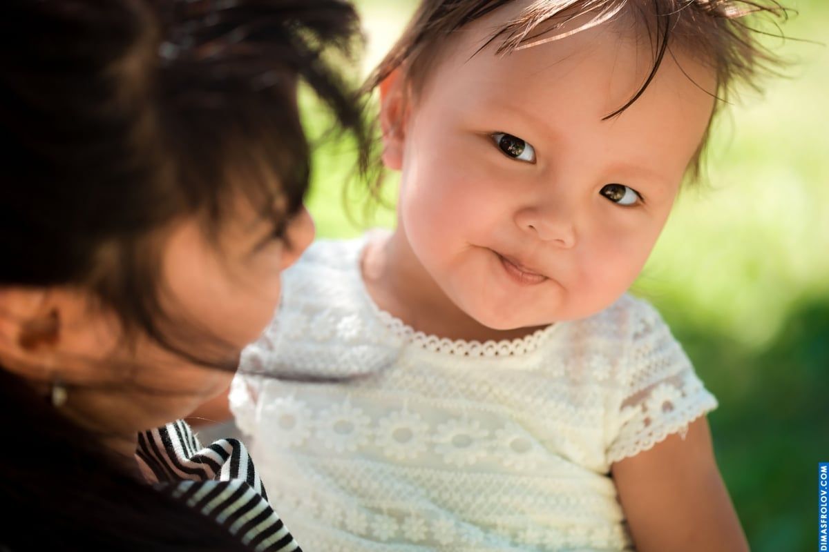 Sweet baby portrait — close-up look with soft smile in mom’s arms