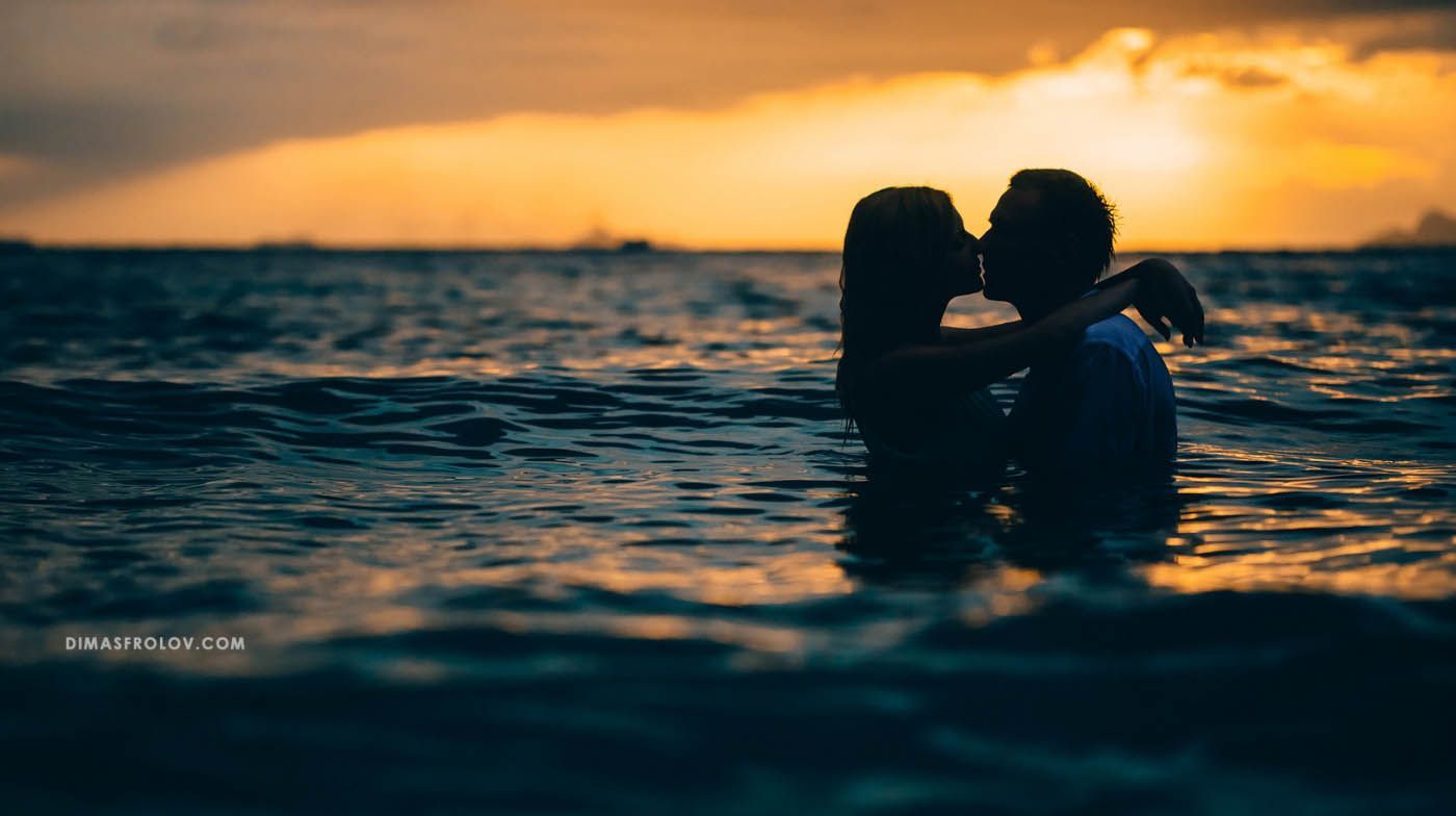 Romantic couple silhouette standing in the sea at sunset
