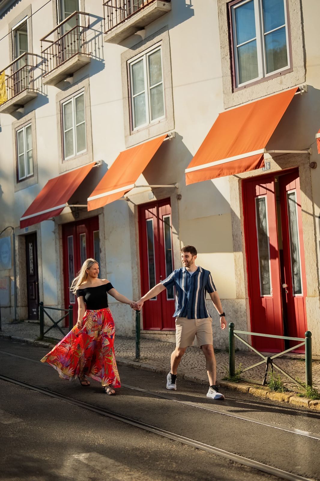 Couple walking hand in hand across the tram tracks on a sunlit Lisbon street