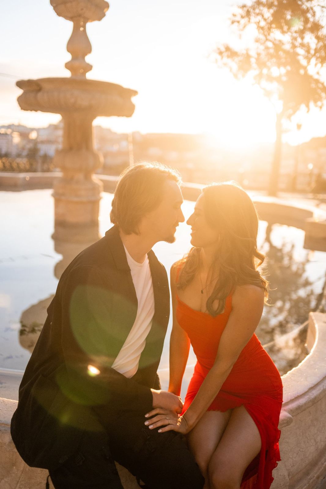 Couple leaning in for a kiss by a stone fountain at golden hour