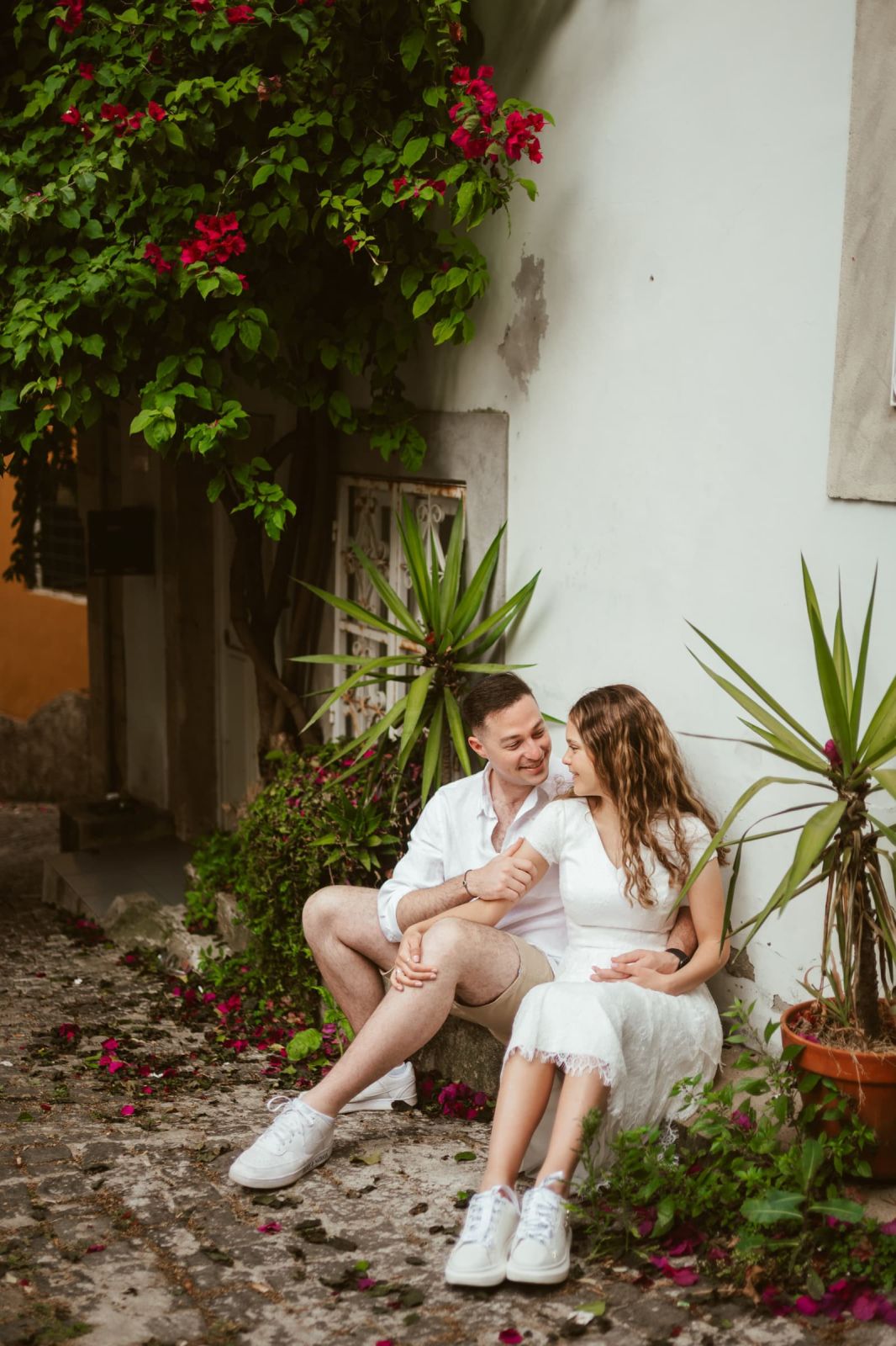 Couple sitting on a cobbled lane under red bougainvillea