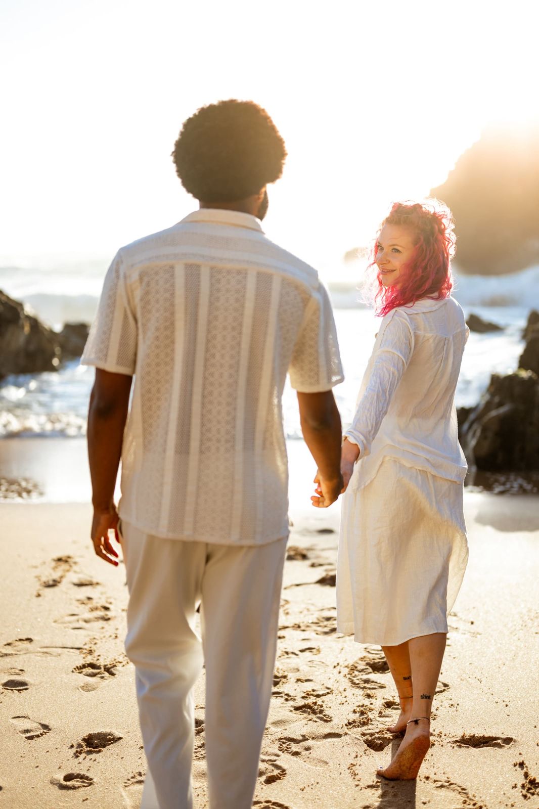 Couple walking away hand in hand on the sand, she looking back over her shoulder