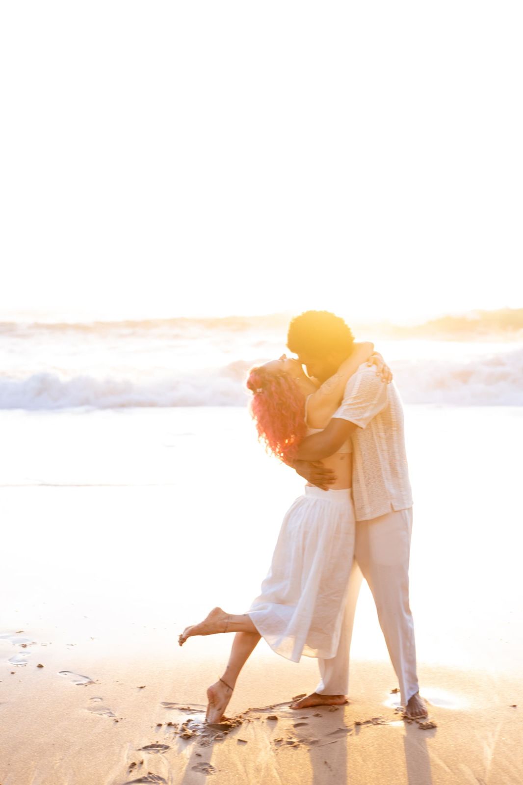 Couple kissing at the water's edge in golden sunset haze