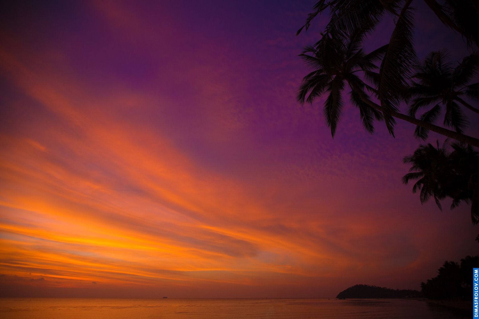 Pôr do sol dramático com nuvens vibrantes em laranja e roxo silhuetando palmeiras contra o céu colorido