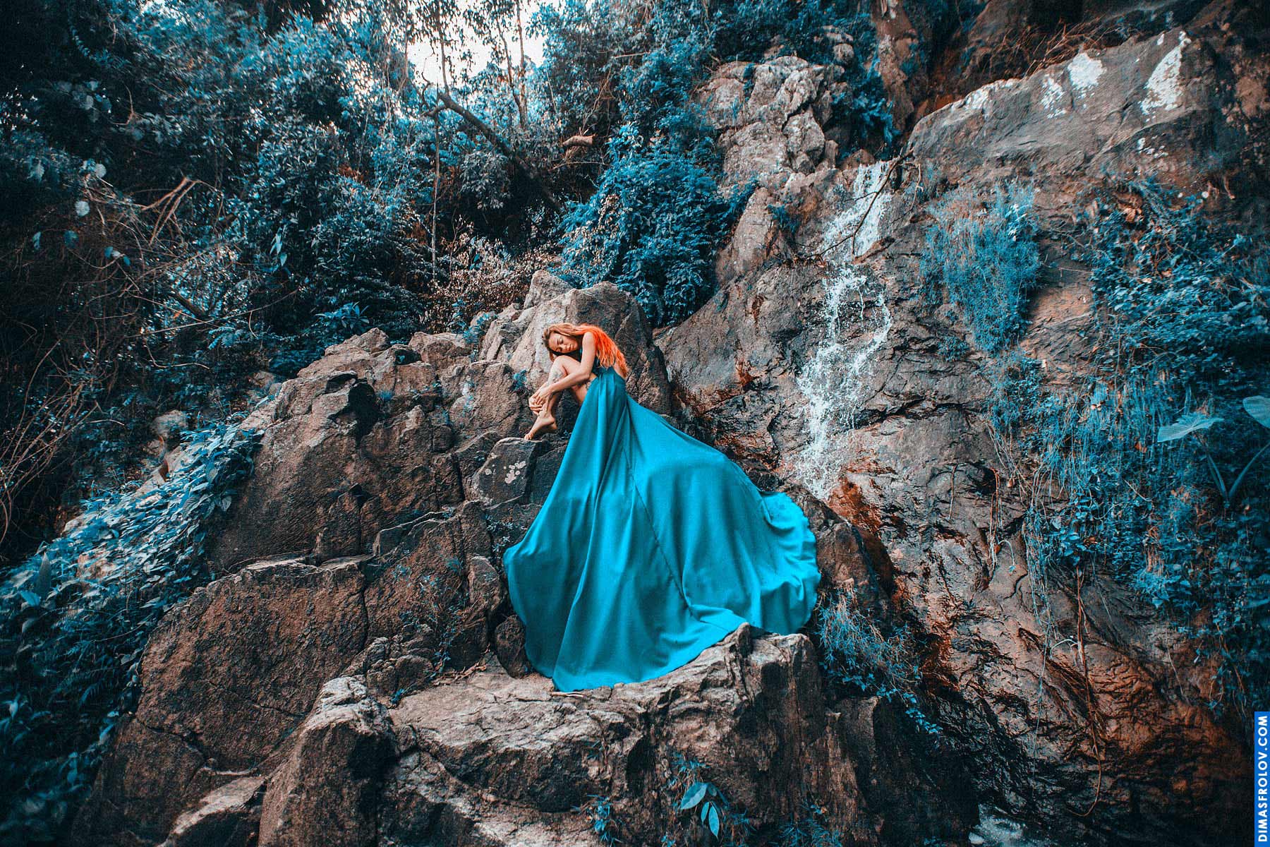 Mystical lady in a long blue gown standing alone among otherworldly rocks