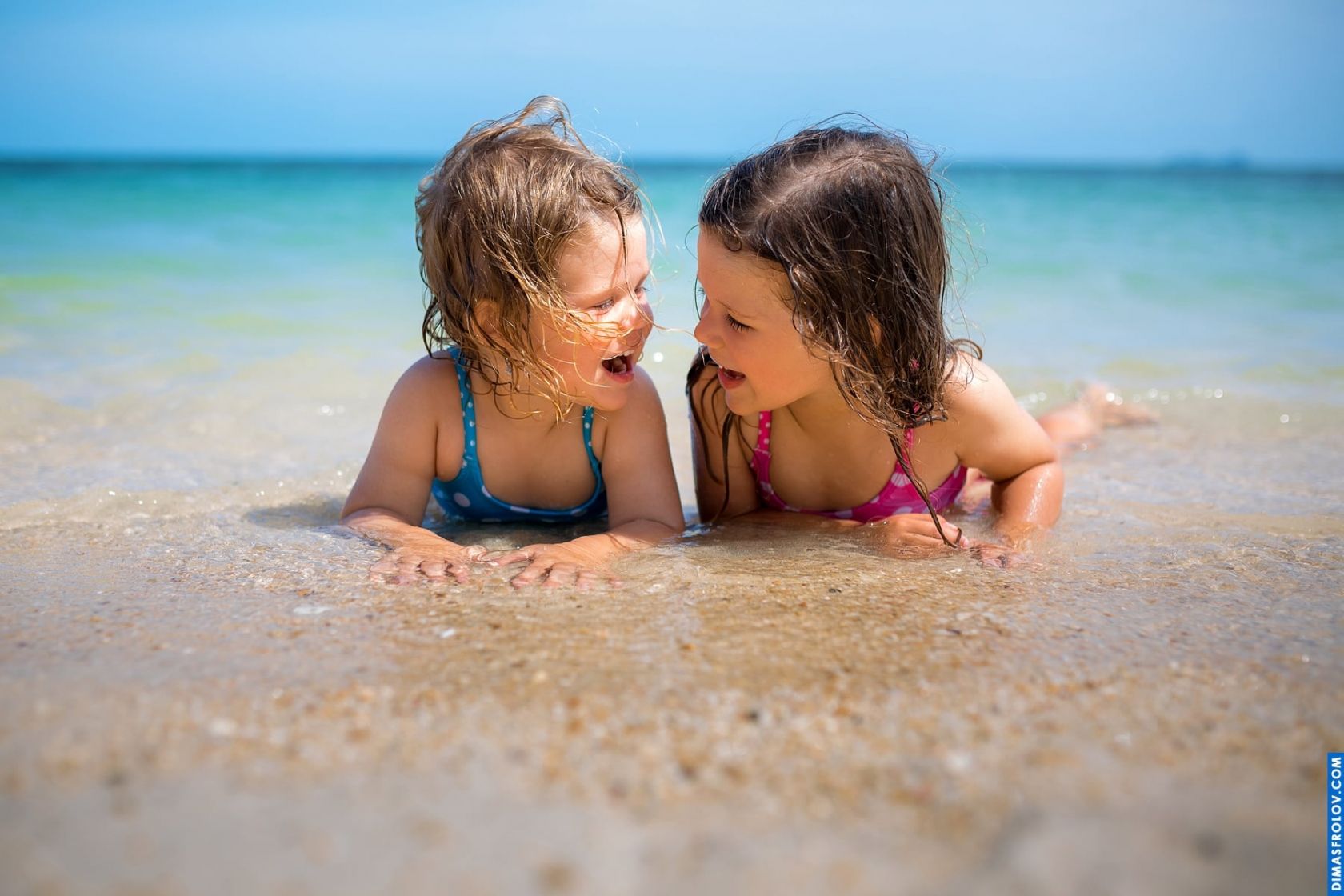 Kids beach photo — two sisters laughing in the sand during a summer photo shoot