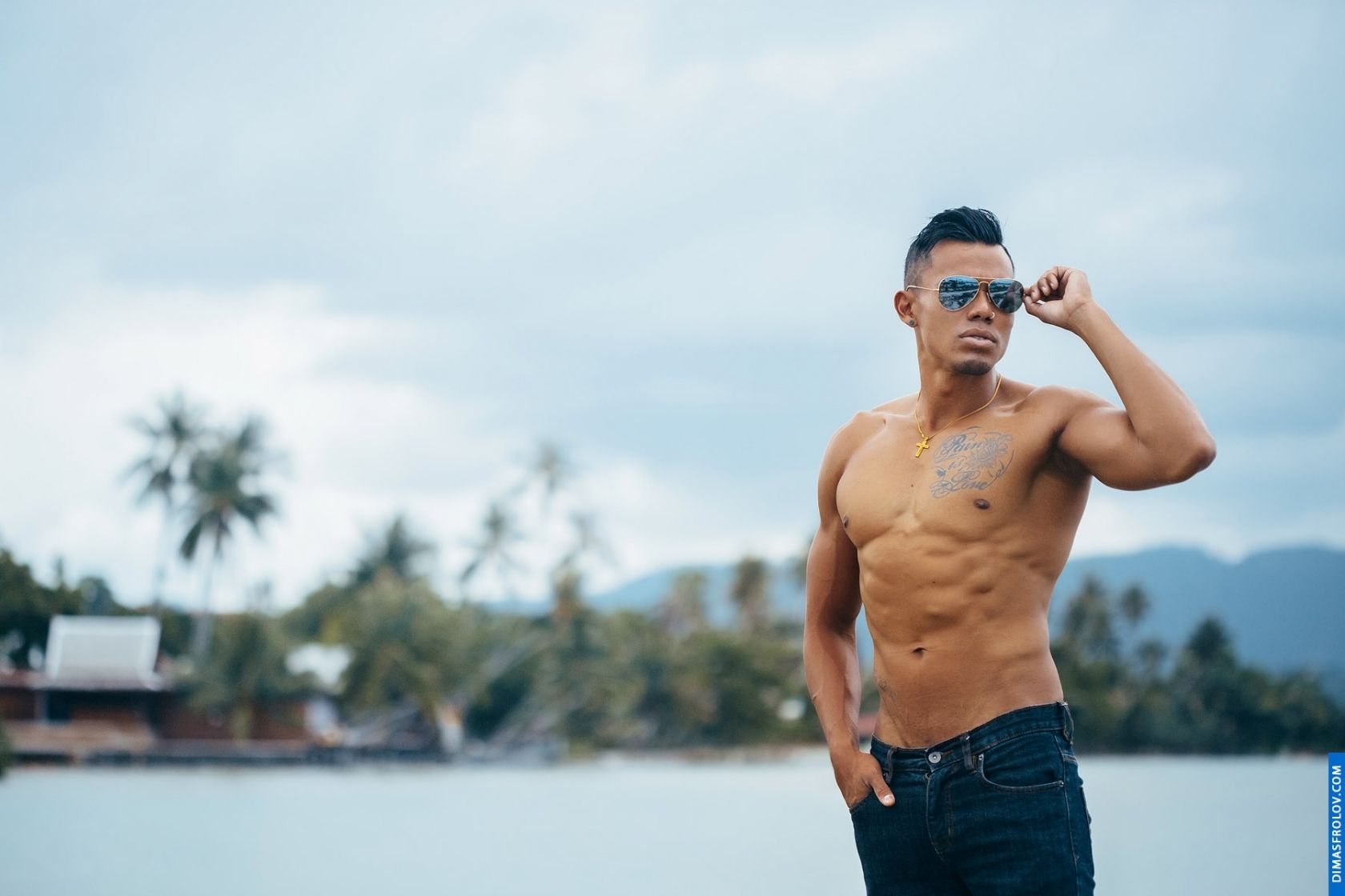 A coastal photo set: a tattooed man in jeans poses by the sea during a bold photo session