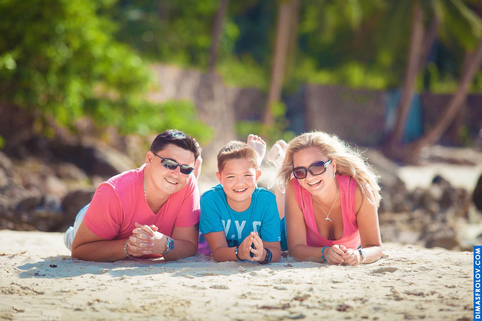 Fun beach portrait — parents with son lying on the sand, smiling together