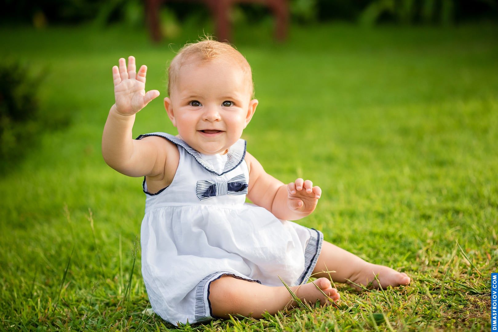 Outdoor baby portrait — waving and smiling while sitting on the grass