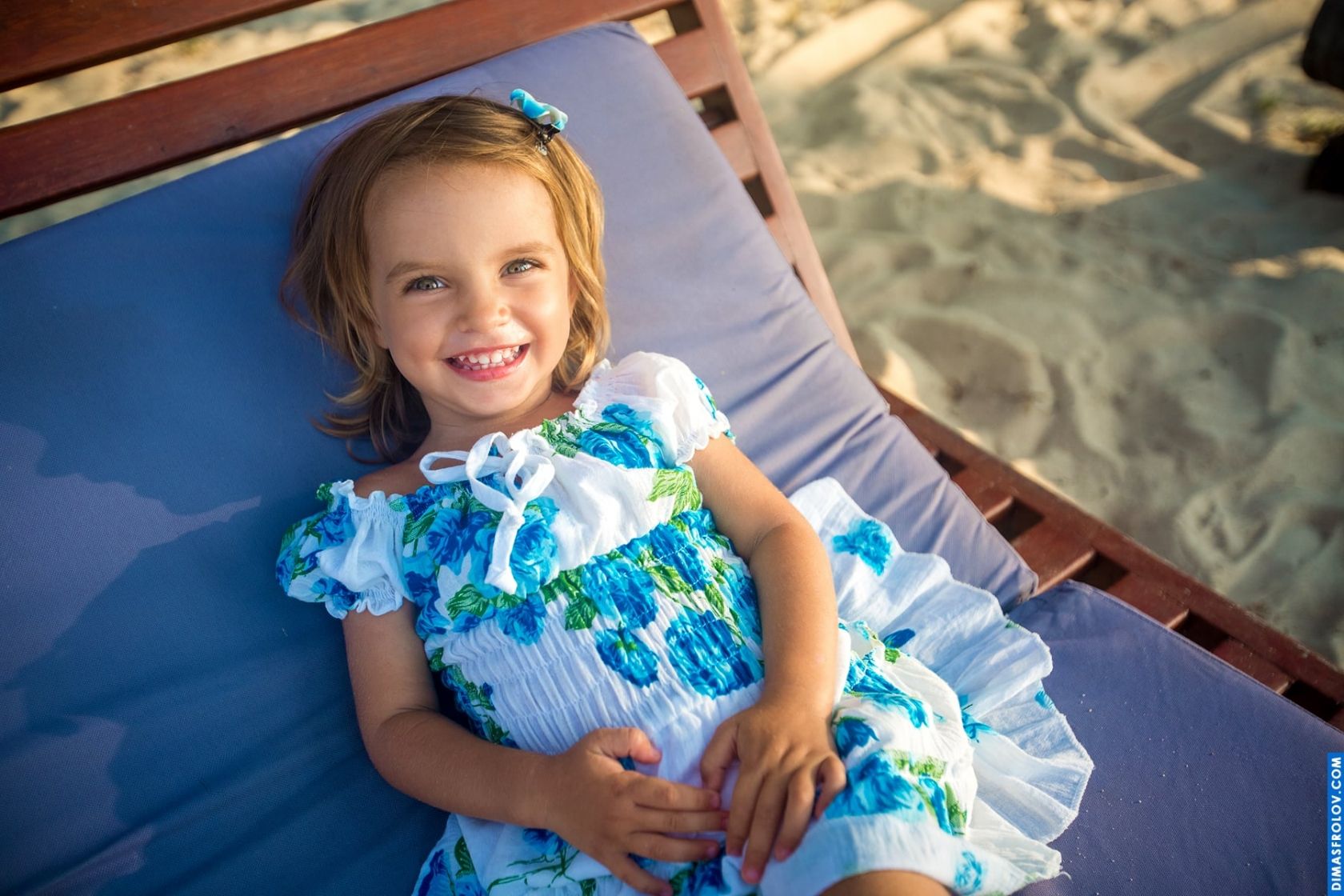 Beach kids photo shoot — smiling girl in a summer dress relaxing in the sun