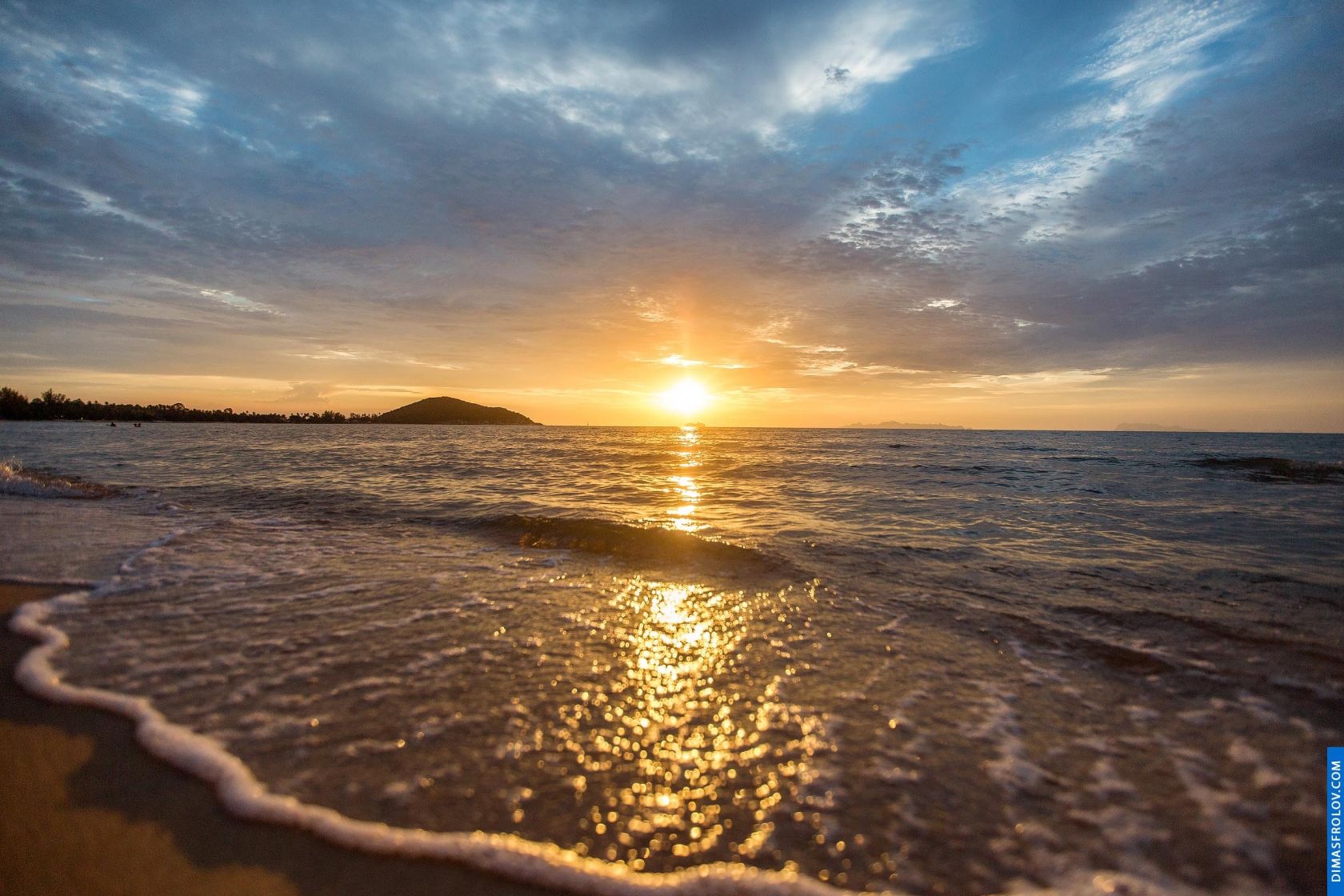 Pôr do sol dourado refletindo em uma praia calma com ondas suaves e um céu parcialmente nublado