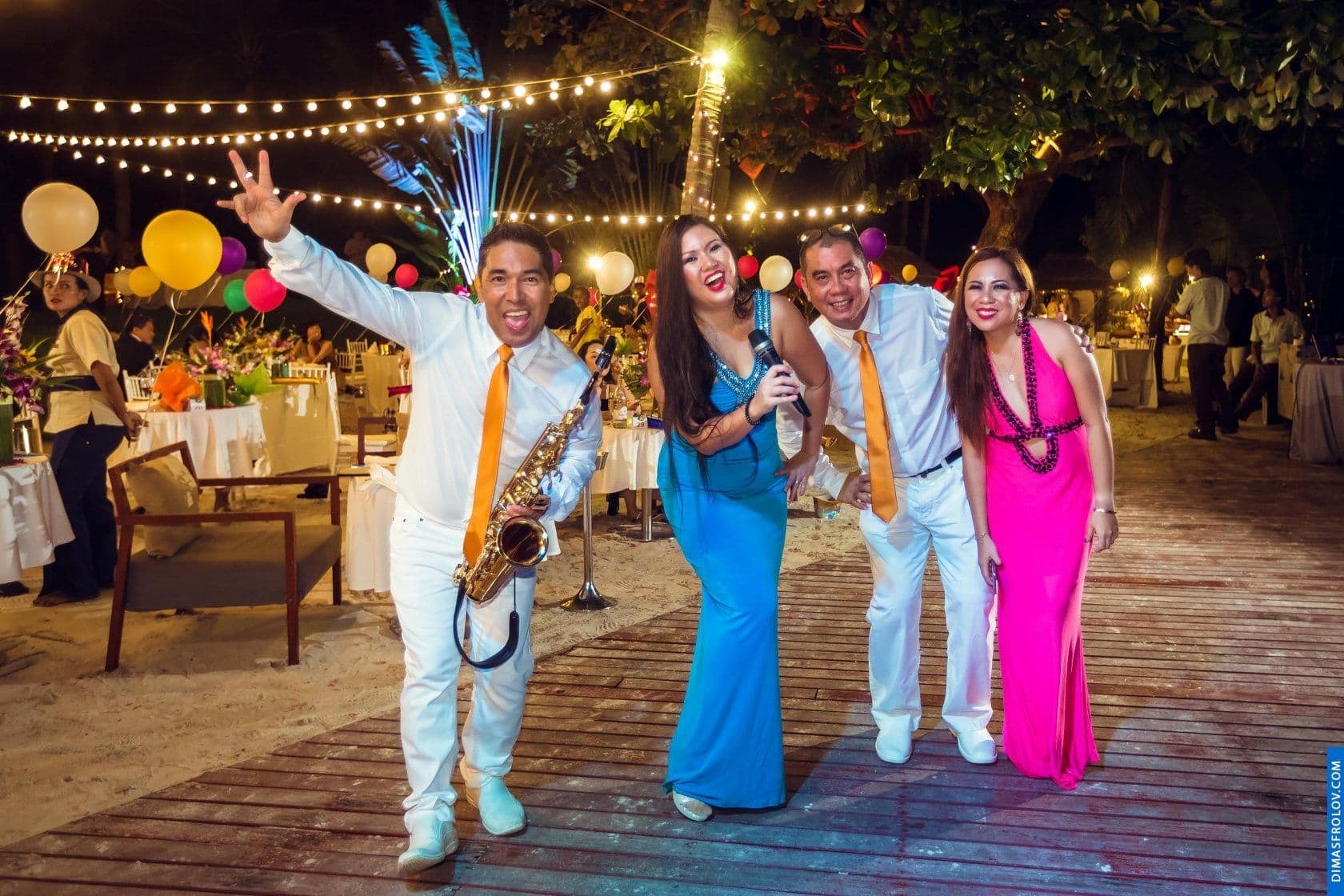 กลุ่มเพื่อนโพสท่าถ่ายรูปและสนุกสนานในงานปาร์ตี้ชายหาดใต้แสงไฟประดับ