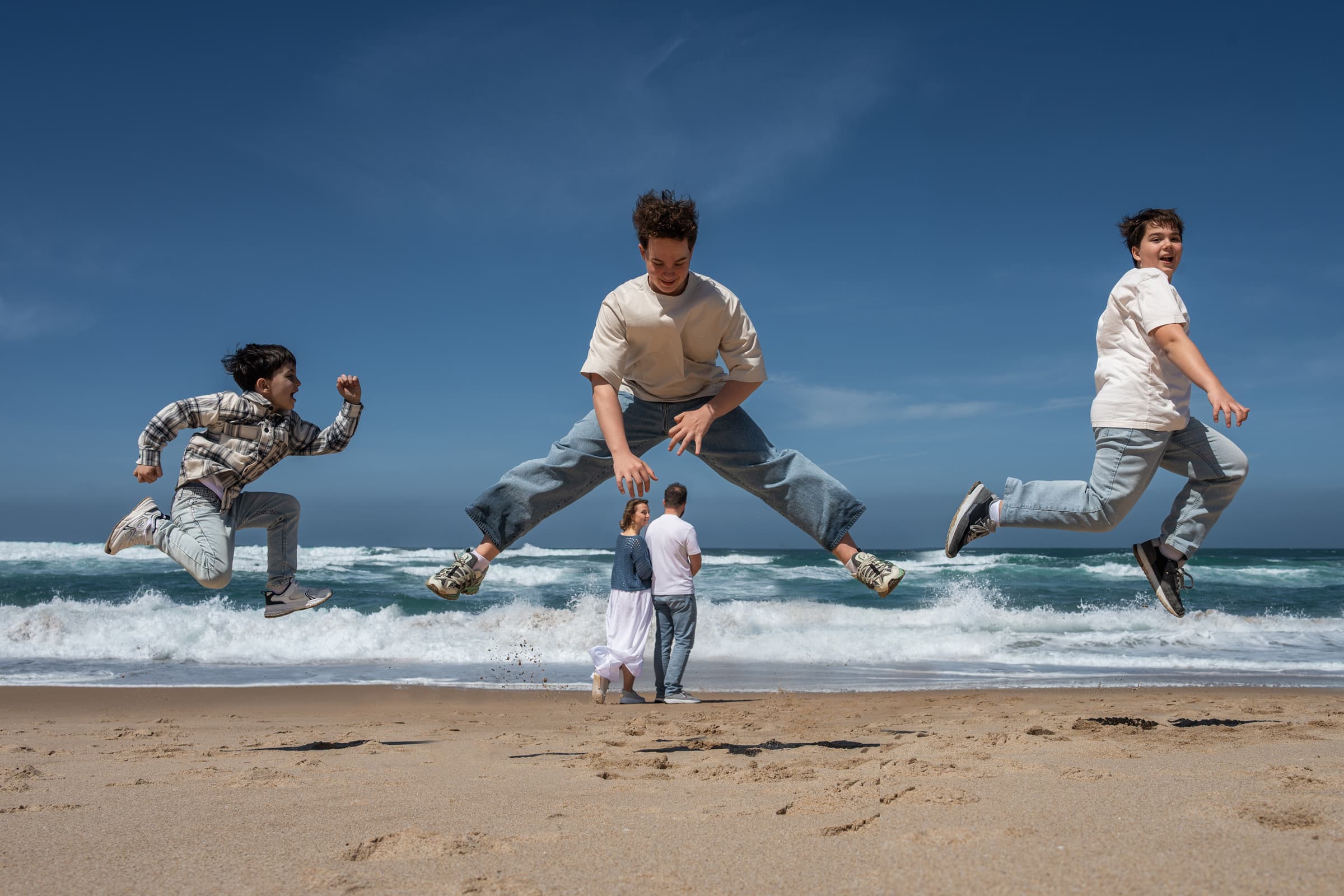 Three brothers jumping on the sand at Guincho beach near Cascais, family photoshoot on the Atlantic coast