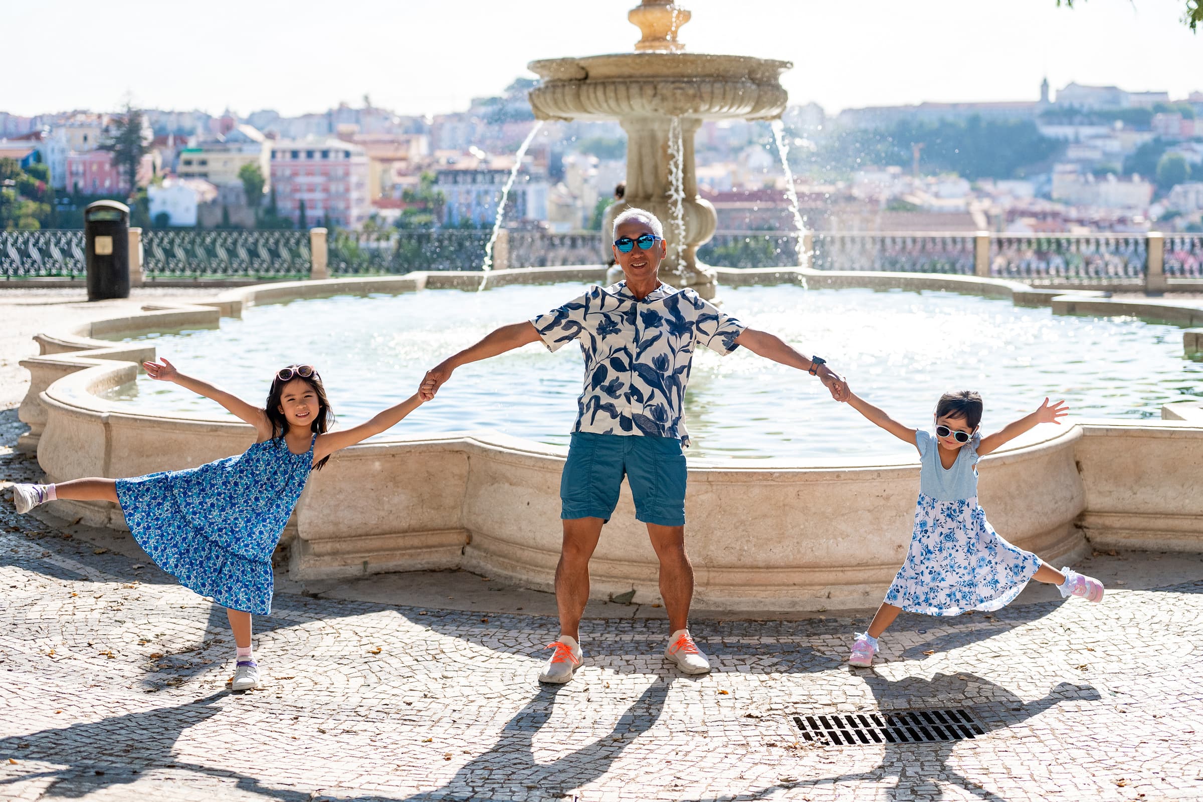 Grandfather and two granddaughters playing by the fountain at Miradouro de São Pedro de Alcântara, family photoshoot in Lisbon
