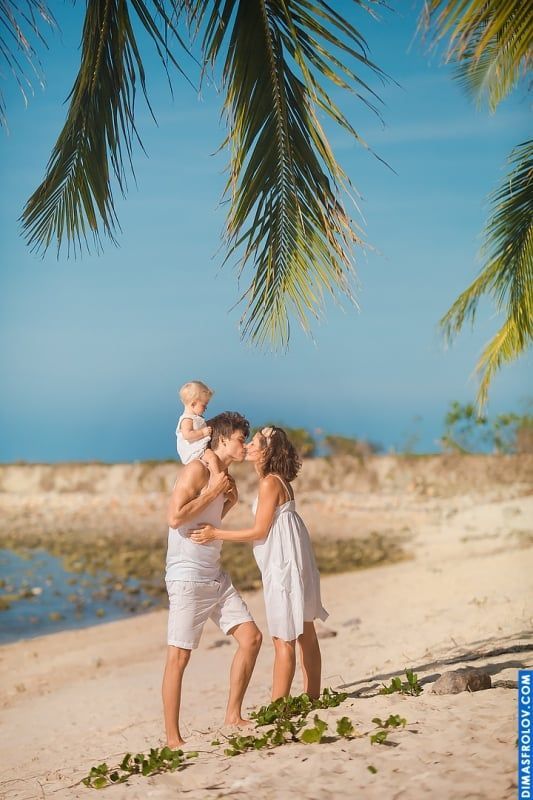 Romantic family photo — kiss under palm trees with baby in arms
