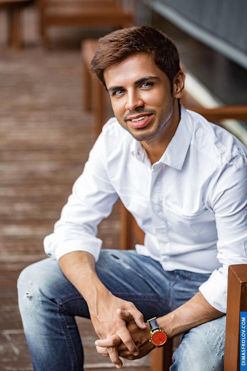 A relaxed indoor portrait: a man in a white shirt sits casually during a calm photo shoot