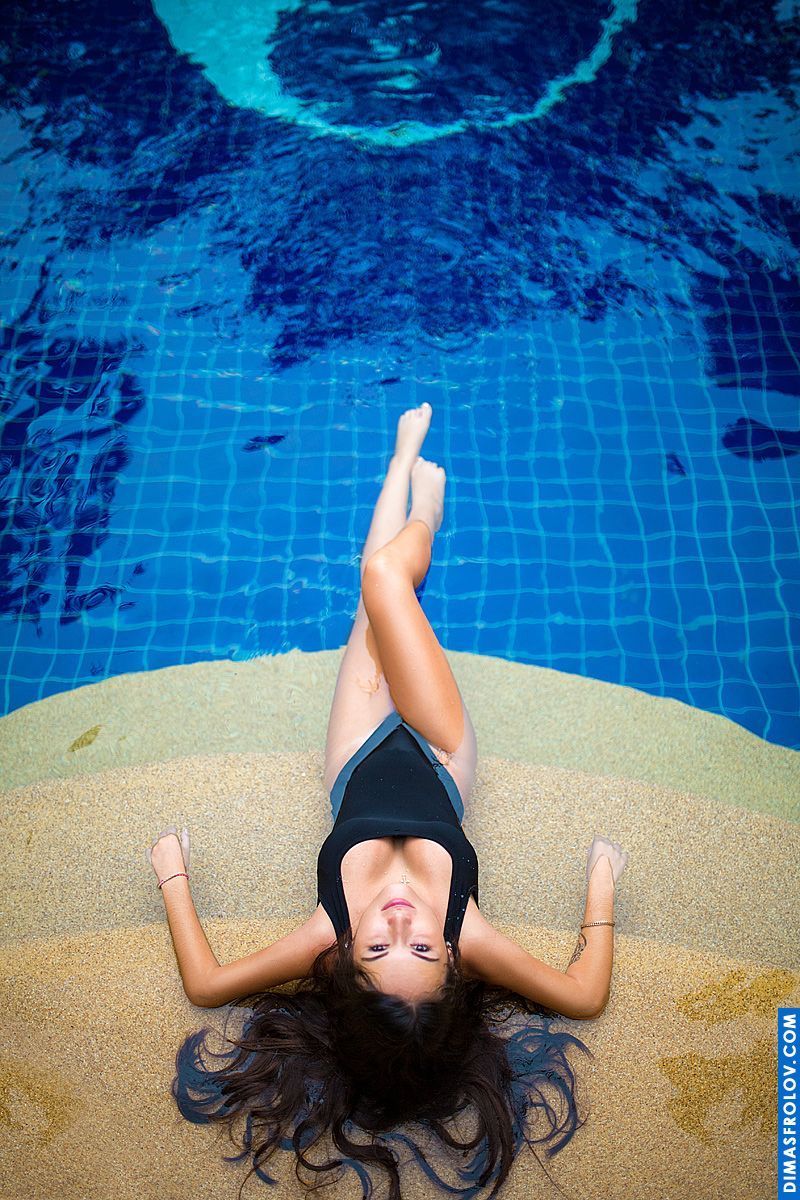 Sessão de moda de banho à beira da piscina com modelo em monokini preto deitado na borda da água azul