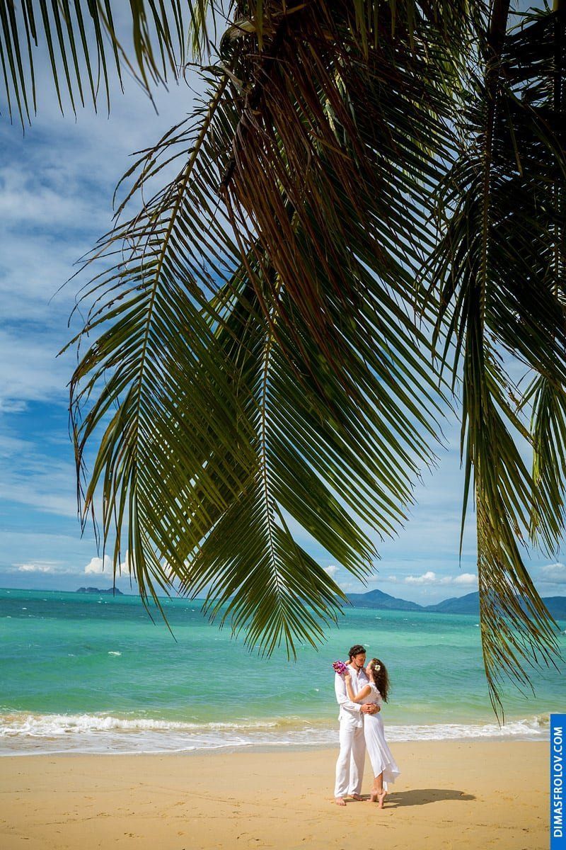 Couple photo shoot on a tropical beach framed by palm leaves